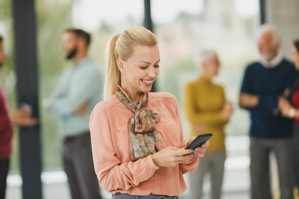 Executiva sorrindo enquanto assina um documento pelo celular, com a equipe ao fundo