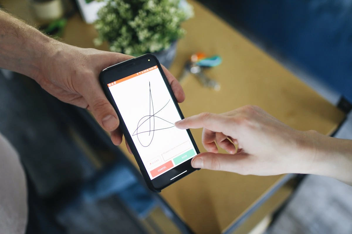 Pessoa segura um smartphone exibindo uma assinatura eletrônica na tela, voltado para outra pessoa, representando o uso de tecnologia para autenticação digital.