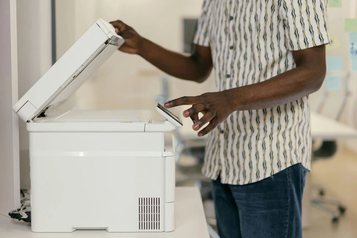 Profissional utilizando impressora multifuncional com scanner para digitalizar documentos físicos, representando o processo de digitalização e gestão documental.