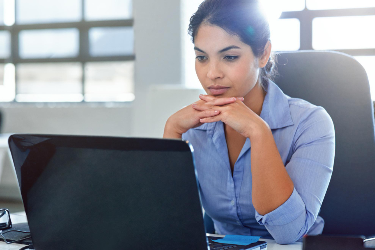 Mulher em ambiente de escritório sentada em frente um notebook lendo sobre: O que é criptografia?
